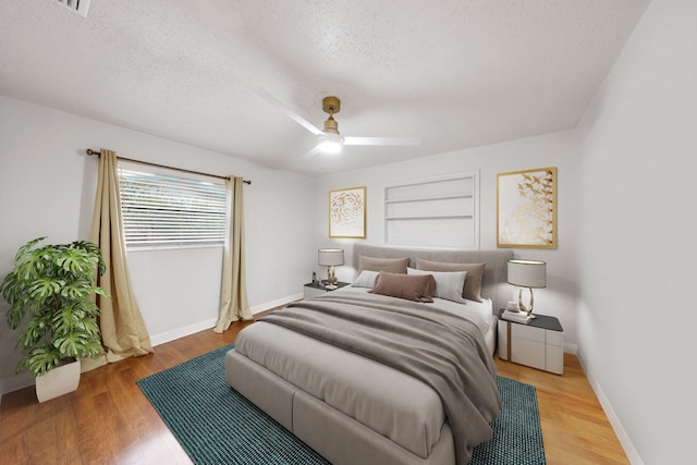 bedroom with ceiling fan, wood-type flooring, and a textured ceiling