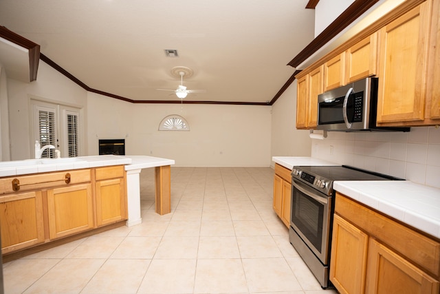 kitchen featuring ceiling fan, tile countertops, crown molding, decorative backsplash, and appliances with stainless steel finishes