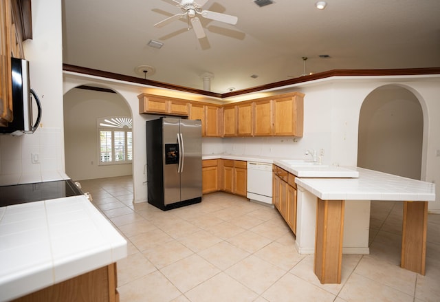 kitchen with dishwasher, kitchen peninsula, ceiling fan, tile counters, and stainless steel fridge with ice dispenser