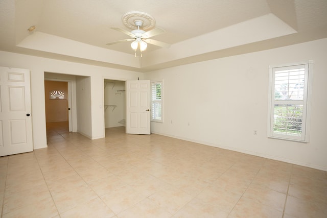 tiled empty room featuring ceiling fan and a tray ceiling