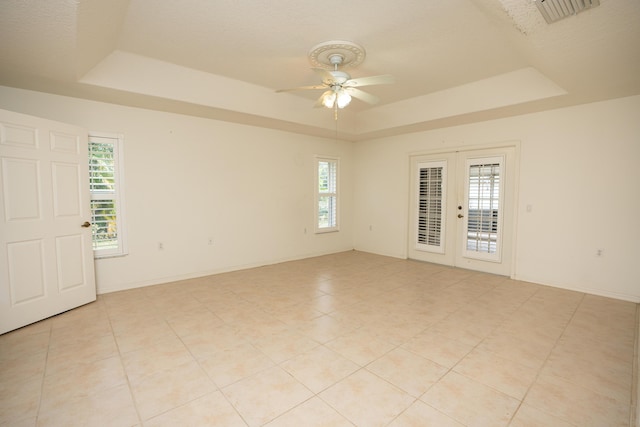 empty room featuring a raised ceiling, french doors, and plenty of natural light