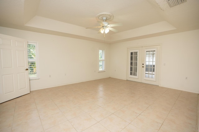 empty room featuring french doors, a raised ceiling, and a healthy amount of sunlight