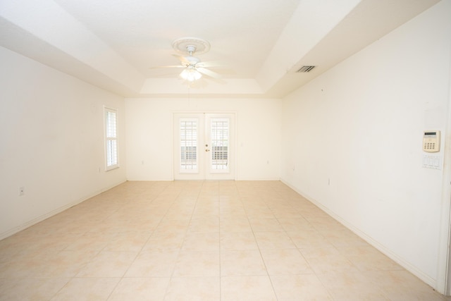 tiled empty room with ceiling fan, french doors, and a tray ceiling