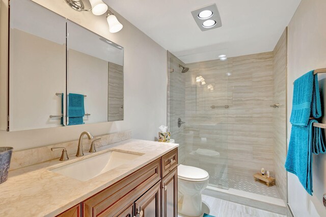 bathroom featuring a tile shower, vanity, and toilet