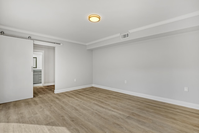 unfurnished room with light wood-type flooring, a barn door, and ornamental molding