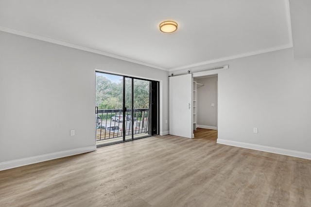 empty room featuring a barn door, light hardwood / wood-style floors, and ornamental molding