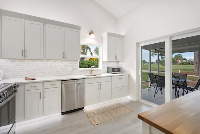 kitchen with sink, stainless steel appliances, high vaulted ceiling, light hardwood / wood-style floors, and white cabinets