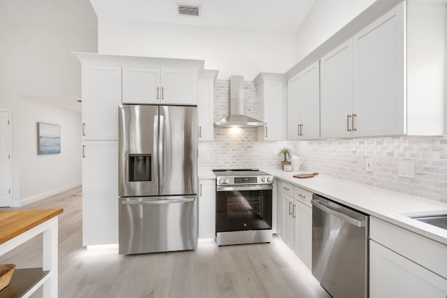 kitchen featuring decorative backsplash, stainless steel appliances, wall chimney range hood, light hardwood / wood-style flooring, and white cabinetry