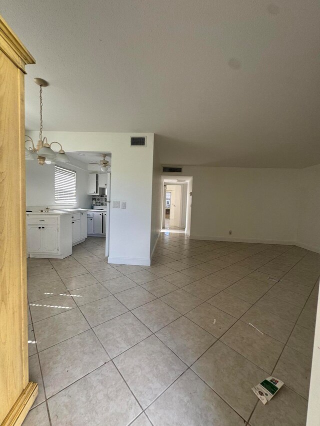 unfurnished living room with a textured ceiling, ceiling fan with notable chandelier, and light tile patterned flooring