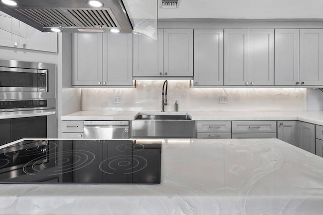 kitchen featuring gray cabinetry, backsplash, stainless steel appliances, ventilation hood, and sink