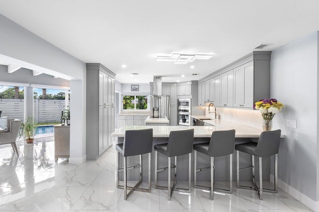 kitchen featuring gray cabinets, a wealth of natural light, kitchen peninsula, and a breakfast bar