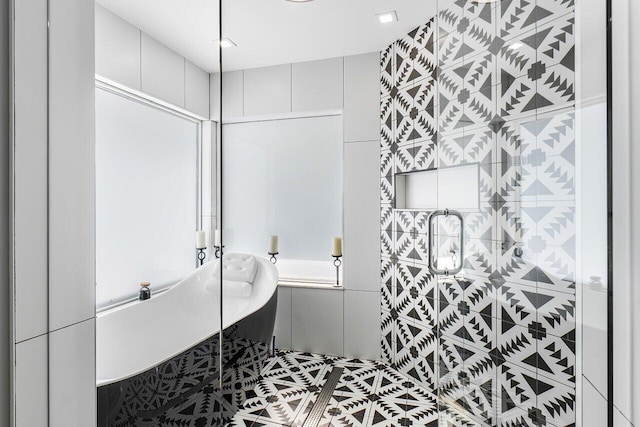 bathroom with tile walls, a tub to relax in, and tile patterned floors