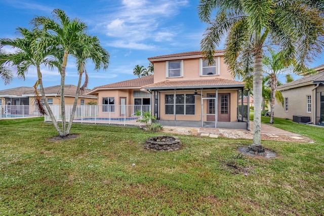 back of property with a sunroom, a yard, ceiling fan, a fenced in pool, and a fire pit