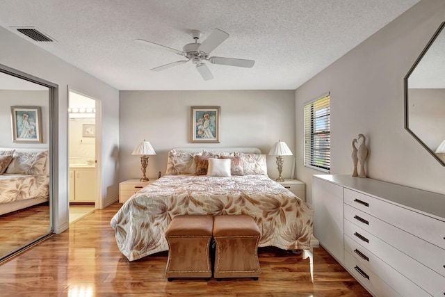 bedroom with ceiling fan, ensuite bathroom, a textured ceiling, a closet, and light wood-type flooring