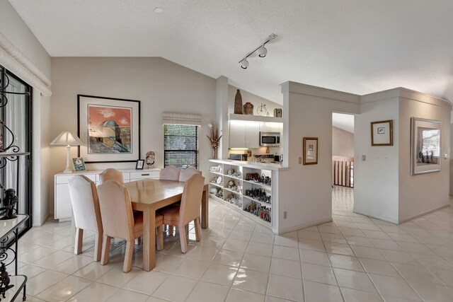 tiled dining space featuring track lighting, vaulted ceiling, and a textured ceiling