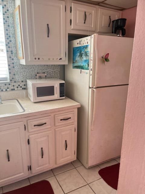 kitchen with backsplash, sink, light tile patterned flooring, white cabinetry, and white appliances