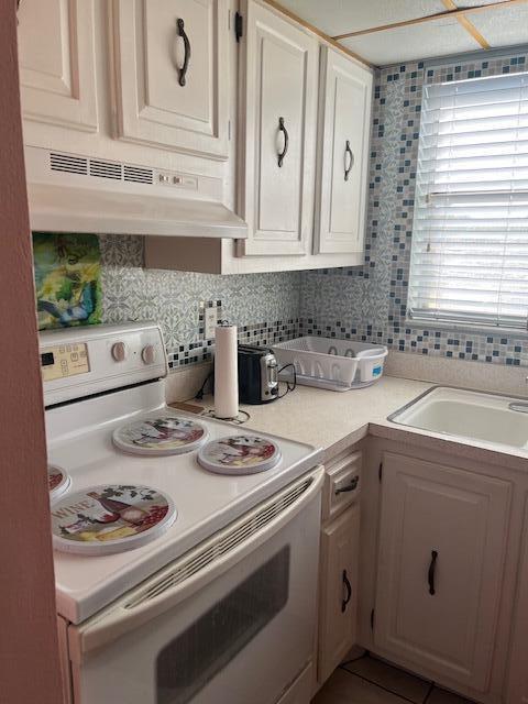 kitchen featuring decorative backsplash, exhaust hood, sink, white electric stove, and white cabinets