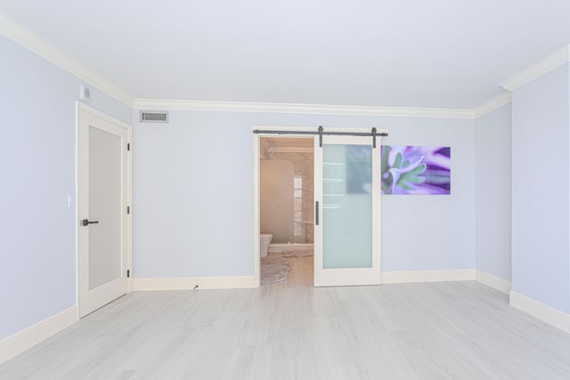 unfurnished room featuring a barn door, crown molding, and light hardwood / wood-style floors