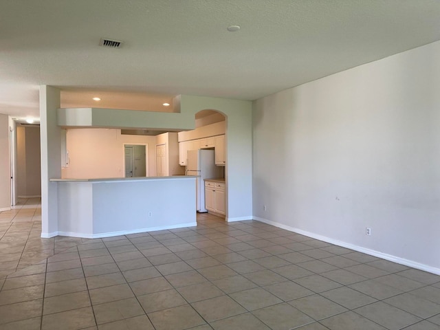 kitchen featuring kitchen peninsula, a textured ceiling, white fridge, and light tile patterned floors