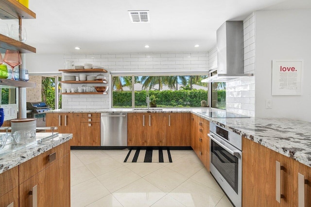 kitchen with light stone countertops, appliances with stainless steel finishes, wall chimney exhaust hood, and a healthy amount of sunlight