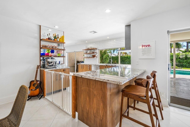 kitchen with kitchen peninsula, light stone counters, sink, light tile patterned floors, and dishwasher