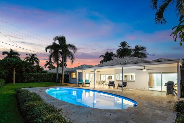 pool at dusk with ceiling fan, a patio area, and grilling area