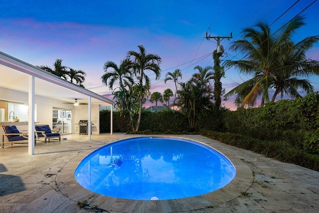 pool at dusk with ceiling fan, sink, a patio, and grilling area