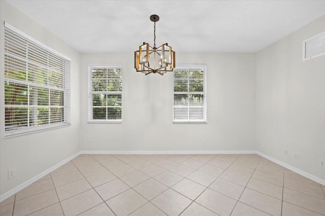 tiled empty room featuring a chandelier and plenty of natural light