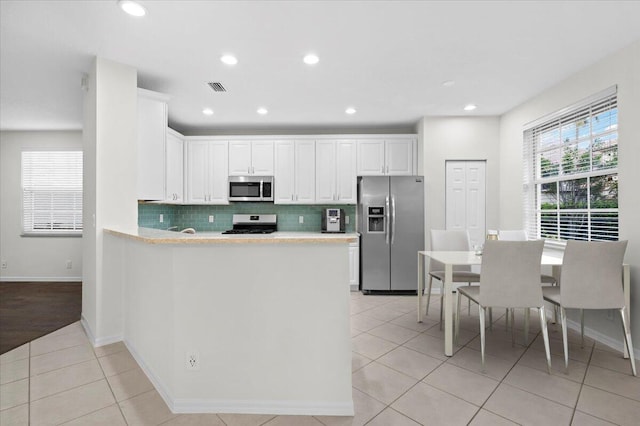 kitchen featuring white cabinets, light tile patterned flooring, appliances with stainless steel finishes, and decorative backsplash