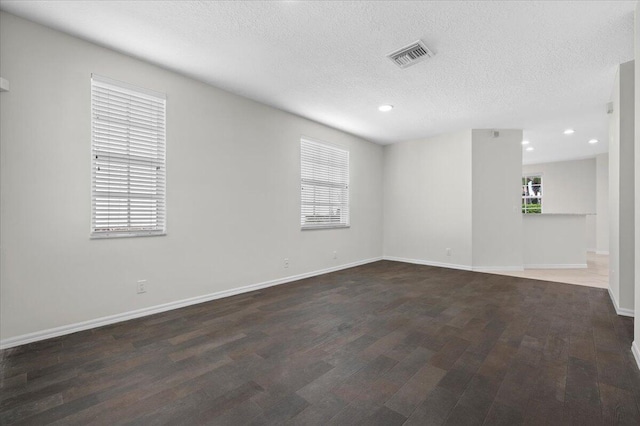 empty room with a textured ceiling, dark hardwood / wood-style flooring, and a wealth of natural light