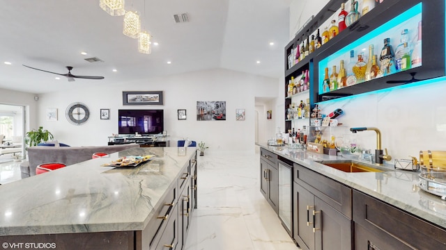 bar featuring ceiling fan, pendant lighting, dark brown cabinetry, sink, and light stone countertops