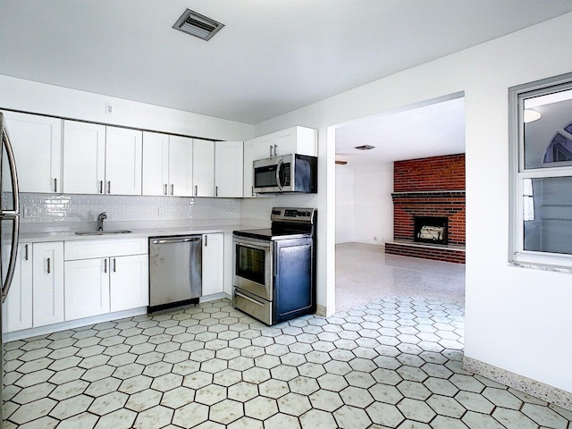 kitchen with a brick fireplace, sink, stainless steel appliances, and white cabinets