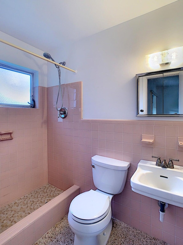 bathroom featuring a tile shower, tile walls, toilet, and sink