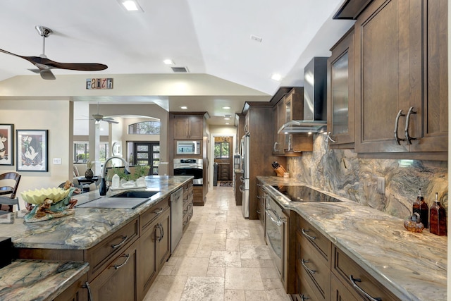 kitchen with appliances with stainless steel finishes, wall chimney exhaust hood, lofted ceiling, and light stone counters