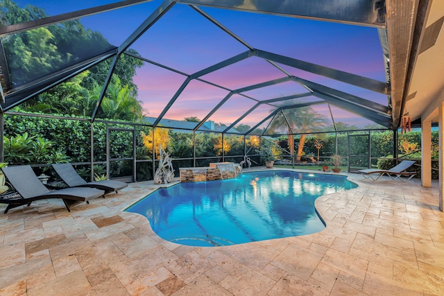 pool at dusk with a patio, a lanai, and pool water feature