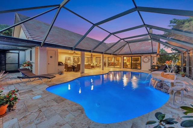 pool at dusk with pool water feature, a patio, and glass enclosure