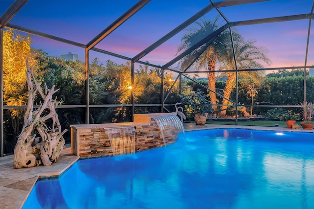 pool at dusk with pool water feature, a lanai, and a patio area