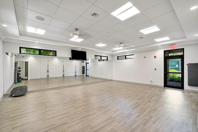 exercise room featuring light hardwood / wood-style flooring, ceiling fan, a raised ceiling, and a paneled ceiling