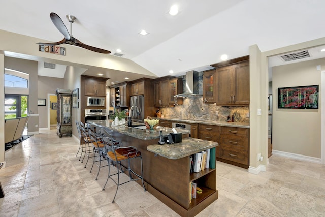 kitchen with tasteful backsplash, wall chimney exhaust hood, appliances with stainless steel finishes, a spacious island, and dark stone counters