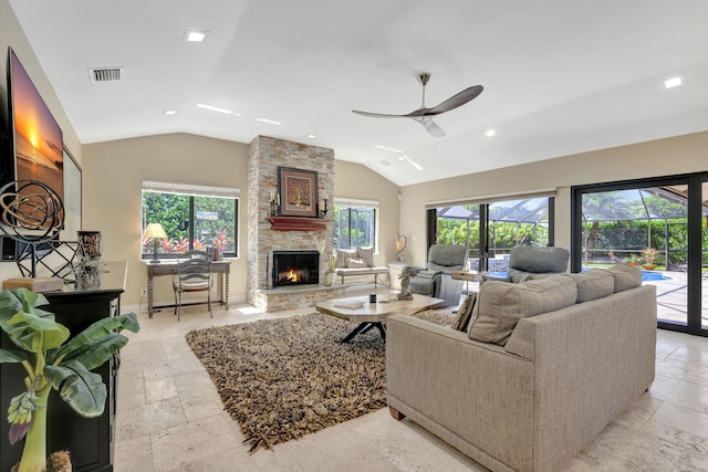 living room featuring lofted ceiling, ceiling fan, and a stone fireplace