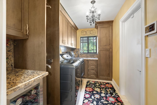 clothes washing area featuring an inviting chandelier, cabinets, washing machine and clothes dryer, and light tile patterned flooring