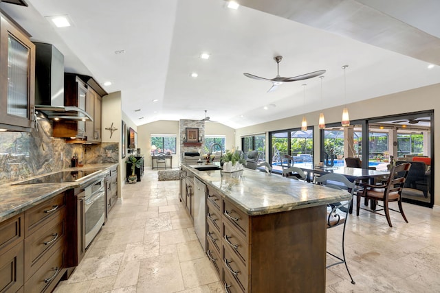 kitchen with pendant lighting, wall chimney exhaust hood, stone counters, a spacious island, and vaulted ceiling