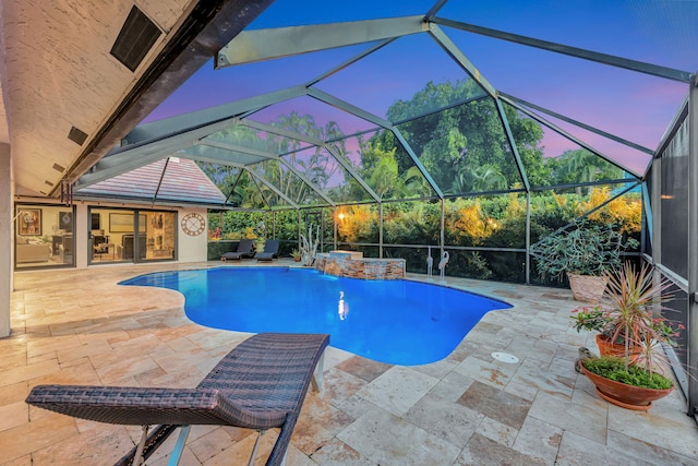 pool at dusk featuring a lanai, pool water feature, and a patio area