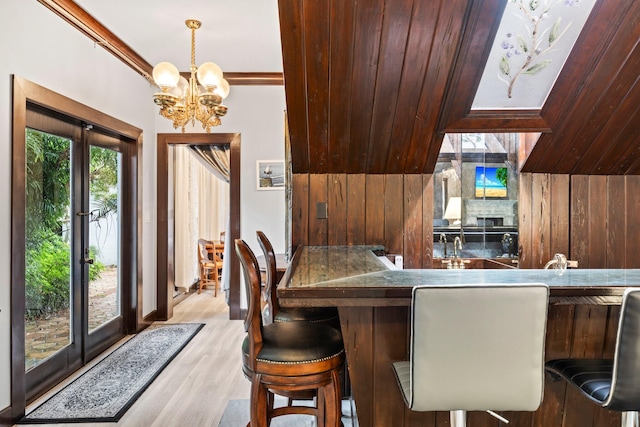 dining space featuring light hardwood / wood-style flooring, ornamental molding, a notable chandelier, french doors, and wooden walls