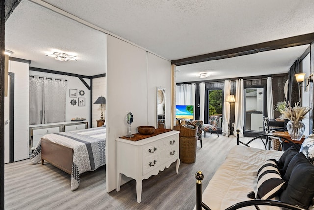 bedroom with beam ceiling, light hardwood / wood-style flooring, and a textured ceiling