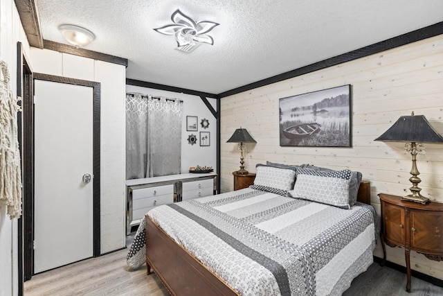 bedroom with wooden walls, a textured ceiling, and light wood-type flooring