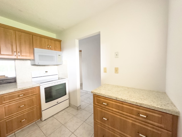 kitchen featuring light tile patterned flooring, light stone countertops, and white appliances