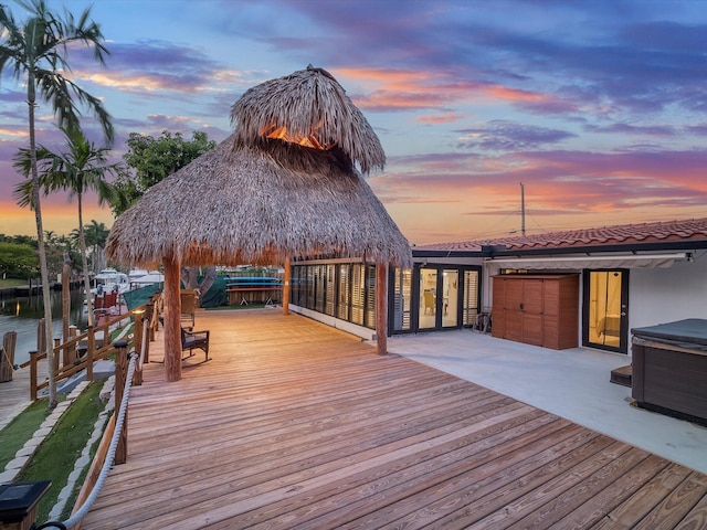 deck at dusk featuring a water view, a patio, and a dock