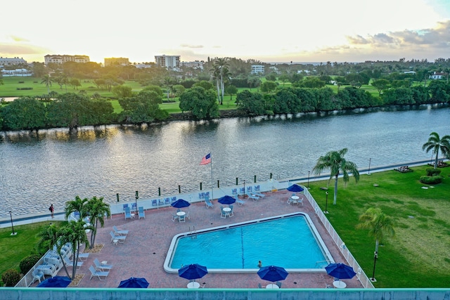 pool at dusk featuring a patio and a water view