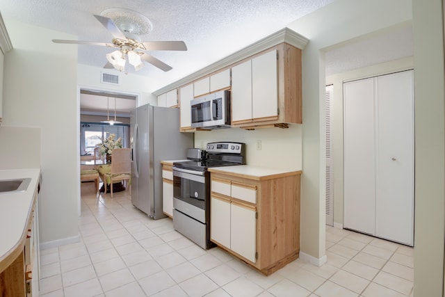 kitchen featuring a textured ceiling, appliances with stainless steel finishes, light tile patterned flooring, and white cabinetry